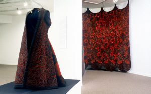 Exhibition with mannequin displaying a red robe and a red textile wall hanging.