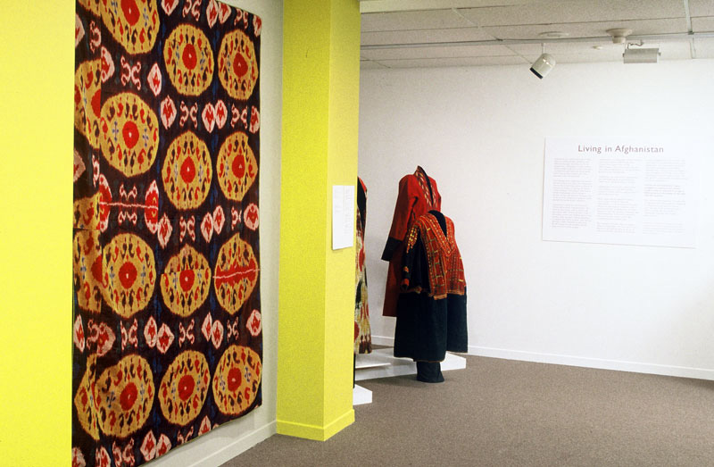 Exhibition with mannequins displaying garments from Afghanistan with textiles hanging from the wall.