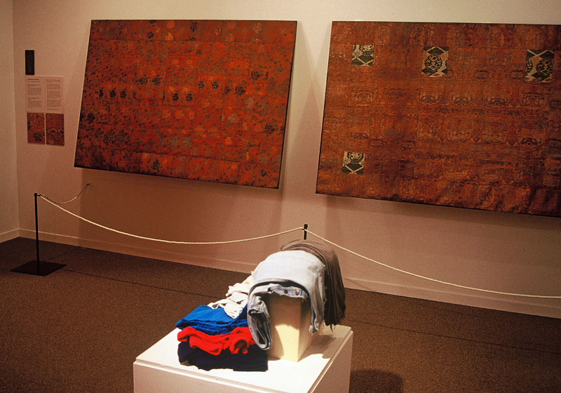 Exhibition with two fabric all hanging and folded clothing on plinth.