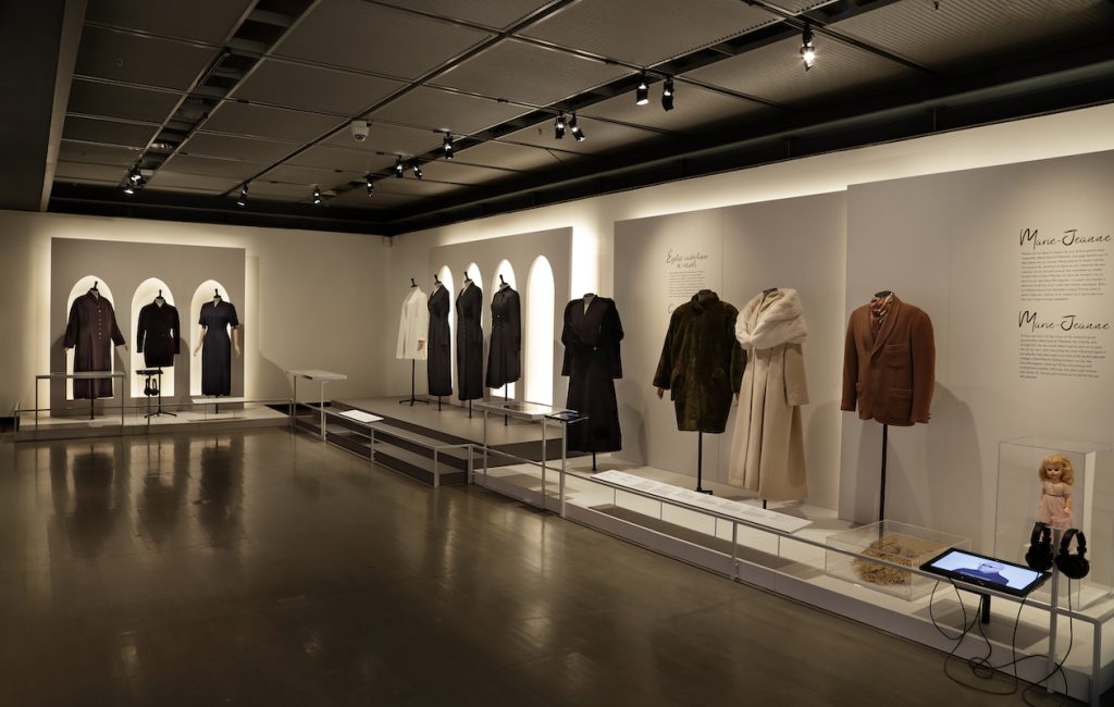 Exhibition with mannequins on plinths against the wall displaying garments.