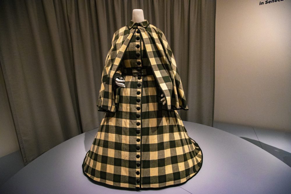 Exhibition with a mannequin on a plinth wearing a yellow and black check ensemble from the 20th century.