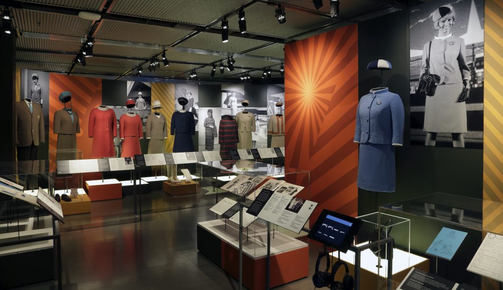 Exhibition with mannequins displaying garments with texts panels.