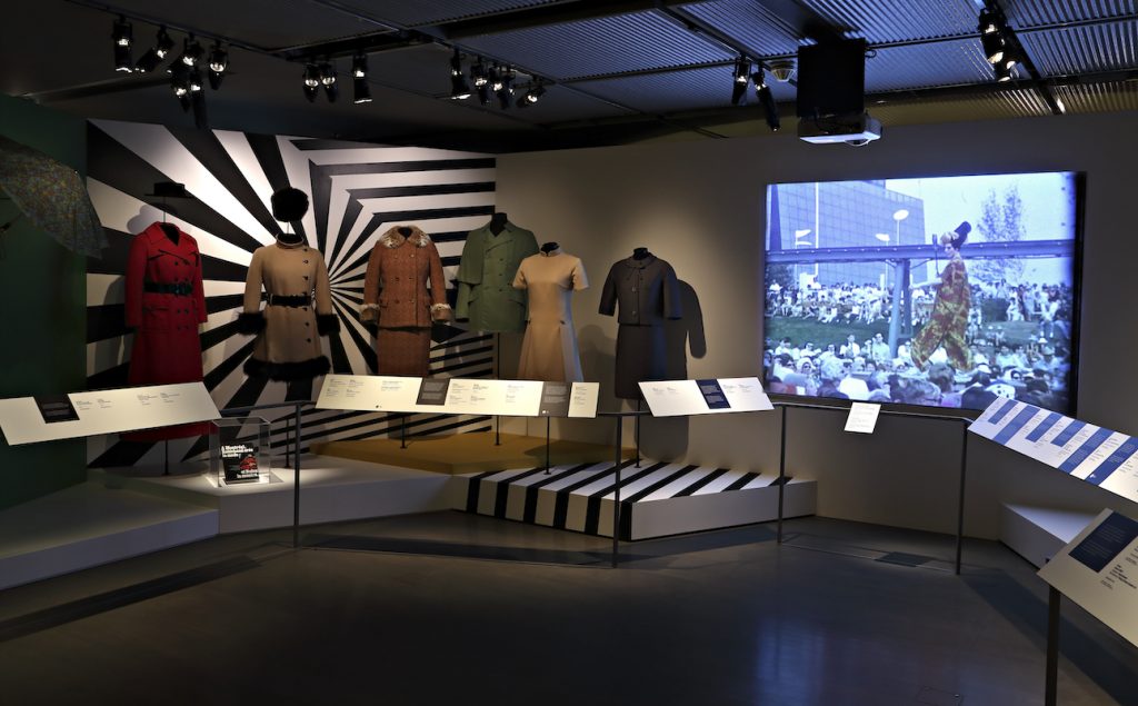 Exhibition with mannequins on plinths displaying garments with television.