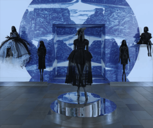 Exhibition with five mannequins displaying black garments; one on a plinth on the floor; two on mirrored plinths next to wall; and two mounted to the wall.