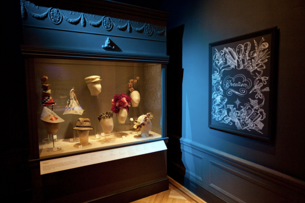 Exhibition with glass cabinets against wall displaying hats.