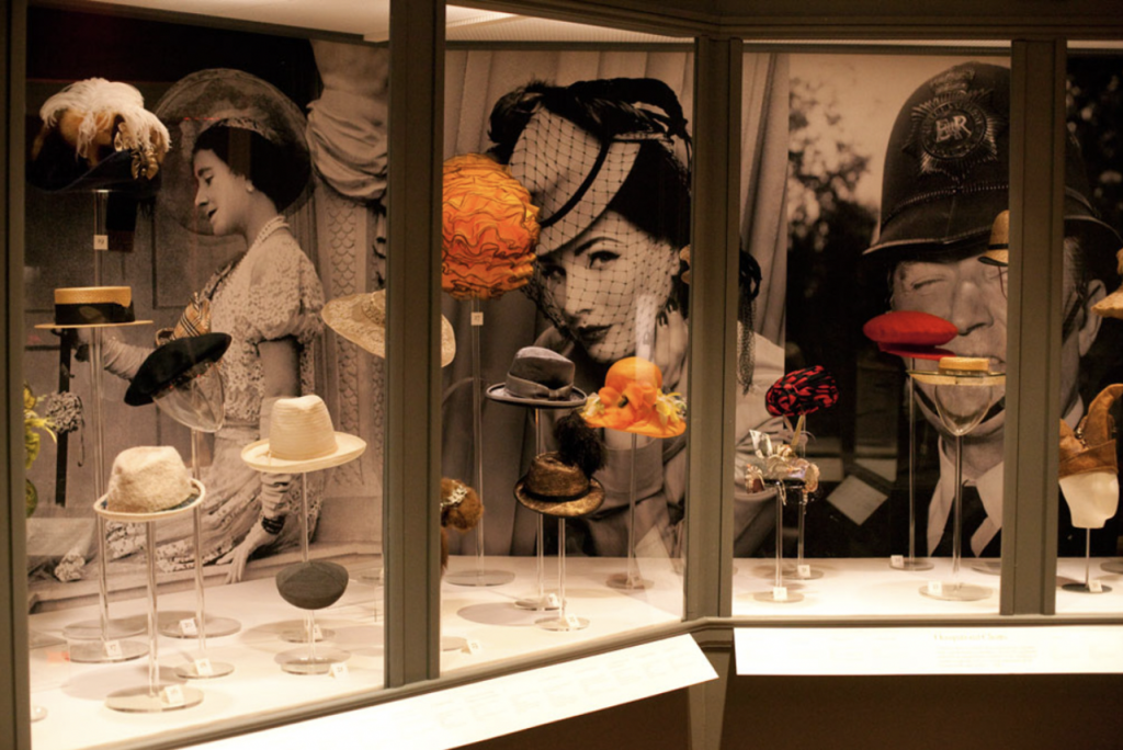 Exhibition with glass cabinets against wall displaying hats.