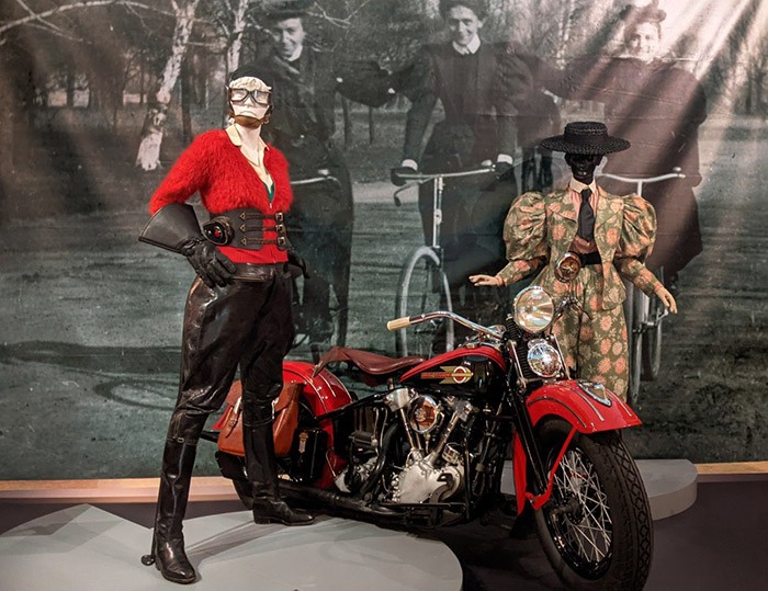 Exhibition with two mannequins displaying motorcycle outfits and one motorcycle.