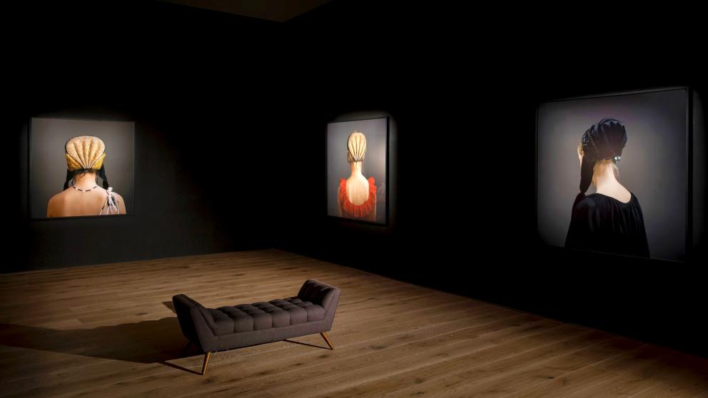 Exhibition with three images on two walls in a dimly lit room.