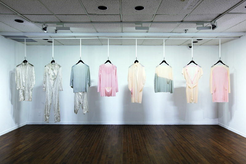 Exhibition with coat hangers hanging from the ceiling with string displaying garments.