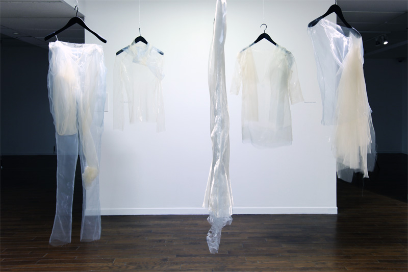 Exhibition with coat hangers hanging from the ceiling with string displaying garments.