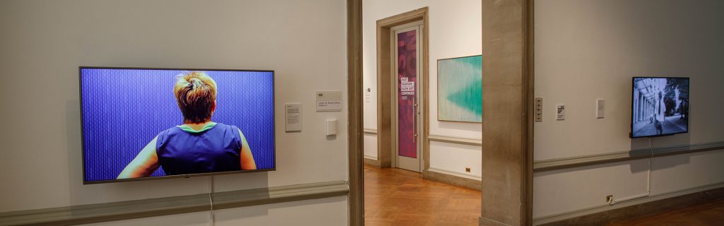Exhibition with two television screens and doorway to another room.
