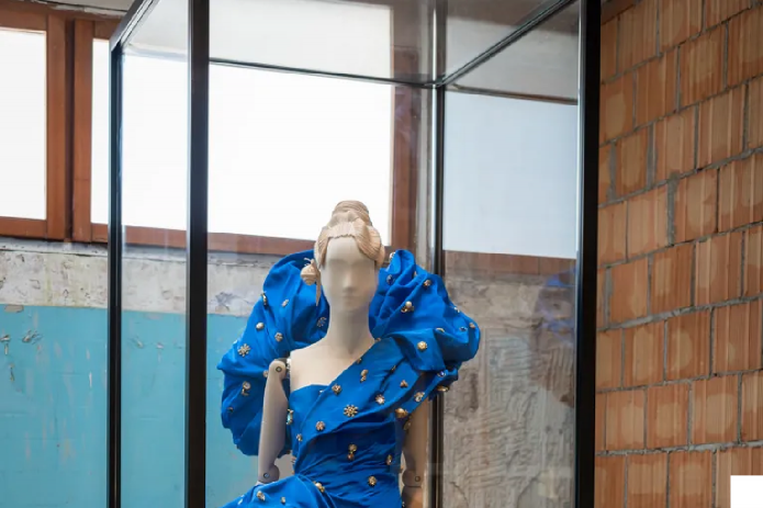 Exhibition display with mannequin in blue dress off the shoulder dress with ruff