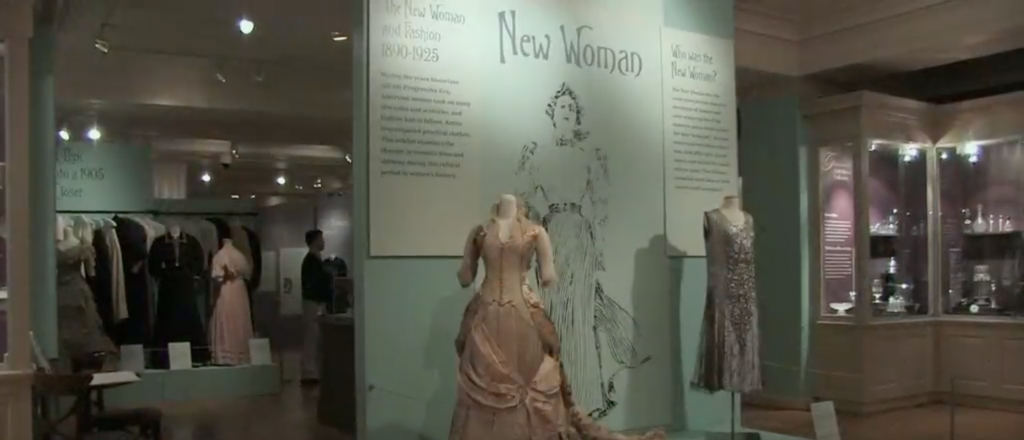 Exhibition with exhibition title on the wall and two mannequins displaying garments.