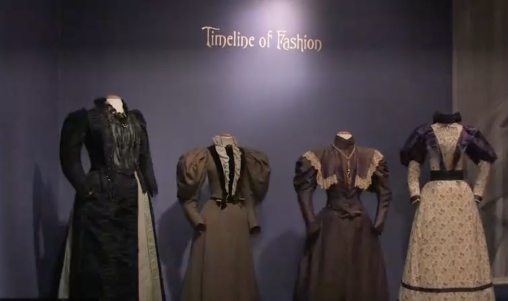 Exhibition with text reading Timeline of Fashion on the wall and mannequins displaying garments.