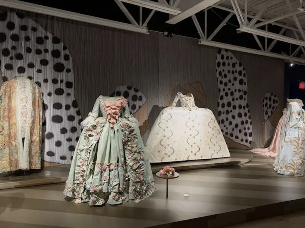 Exhibition with a decorative wall and a plinth holding four mannequins displaying paper garments