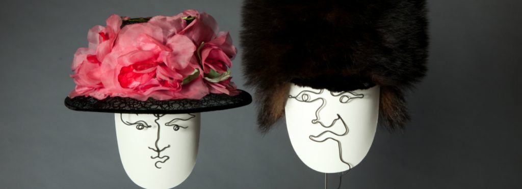 Exhibition with two hat stands with wire shaped as faces displaying hats.