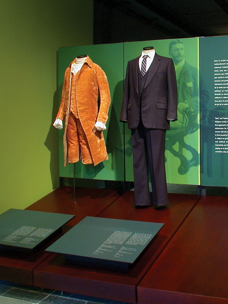 exhibition display of mannequins, one dressed in a amber suit (18th Century?) with breeches and one in a later suit, 20th century
