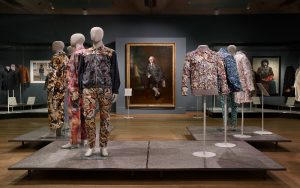 Exhibition display of mannequins in patterned menswear with historic portrait in the background