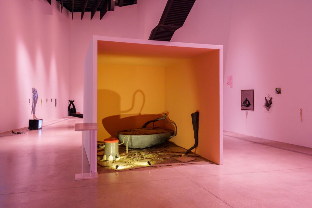 A gallery with large 3 sided box containing surreal objects that appear to be a giant acorn shell and an elephant footstool.