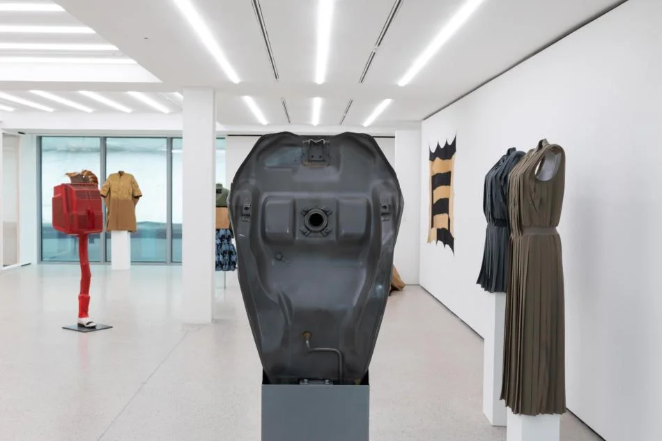 exhibition gallery with grey constructed shape in foreground and dressed mannequins in background