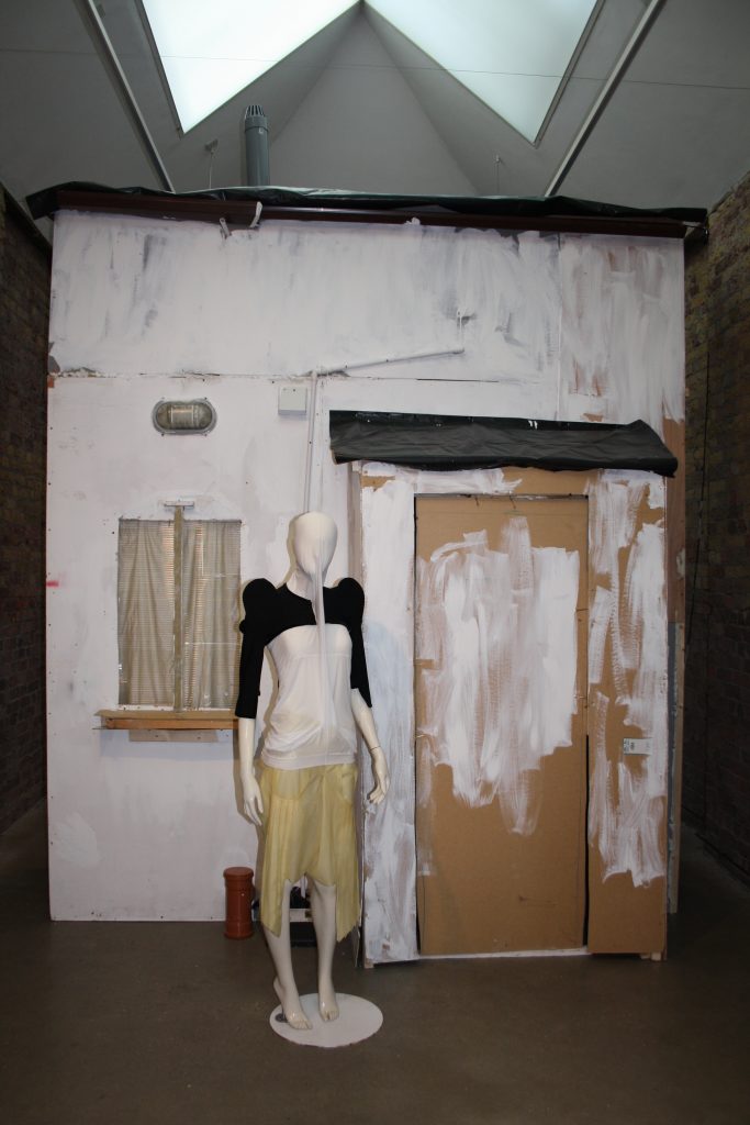 A dressed mannequin in front of a white shed type building