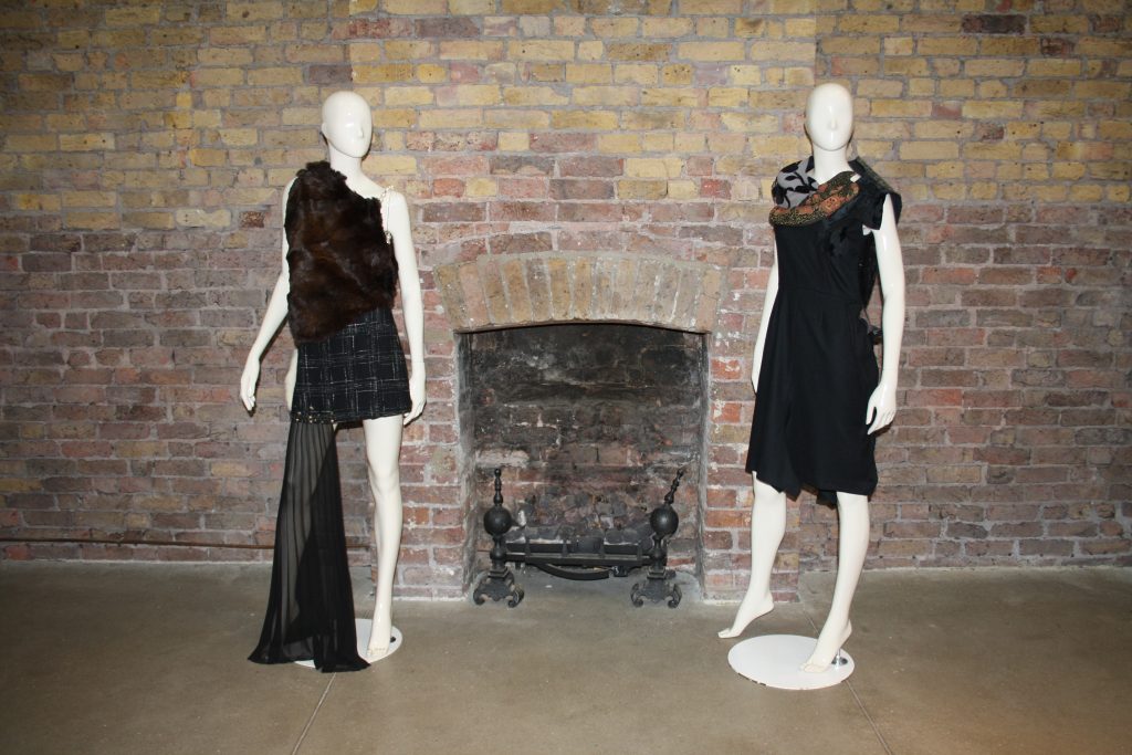 Two mannequins in front of a brick wall with fireplace
