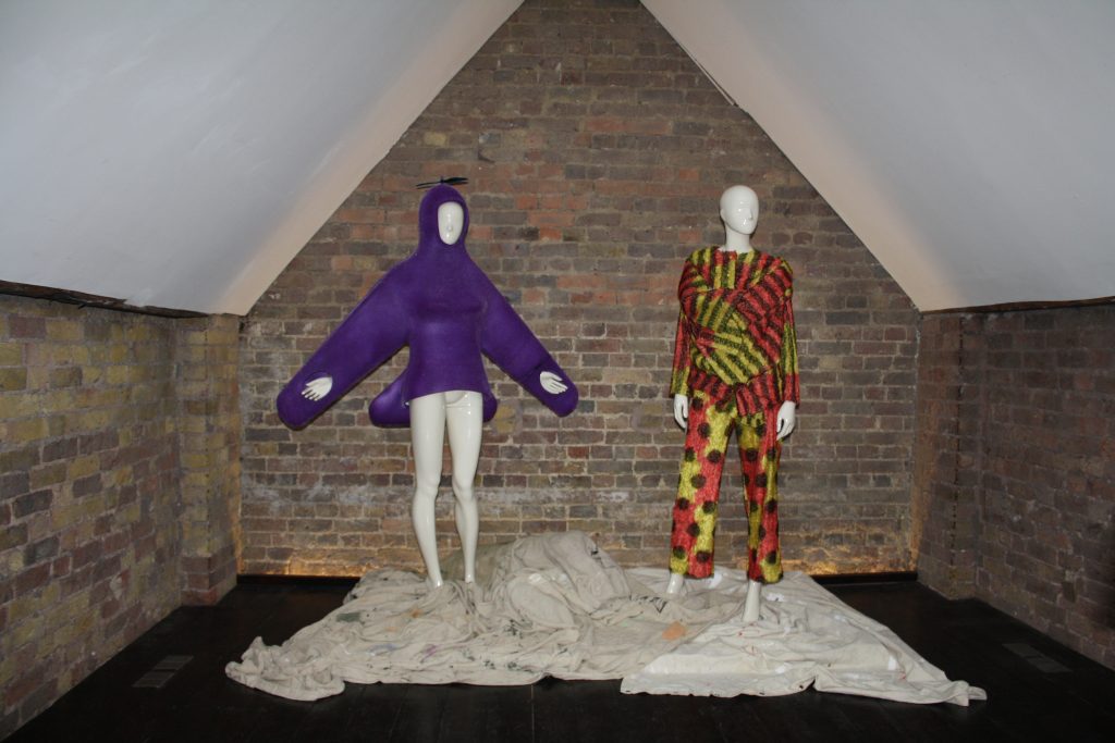 Two dressed mannequins in front of a brick wall under the sloped roof of an attic room