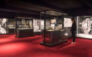 Gallery view of Cartier watches displayed in black-framed cases on a red carpeted floor