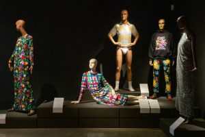 Five mannequins stand and sit in various poses in colourful clothes.