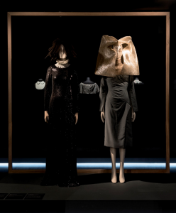 Two dresses with abstract puritan collars stand on white mannequins against a dark backdrop.