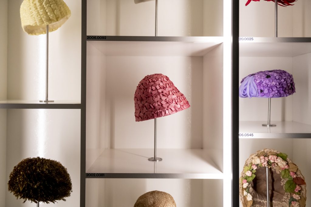 Exhbition view showing some hats, each displayed on differently-levelled shelves forming a wider cabinet.