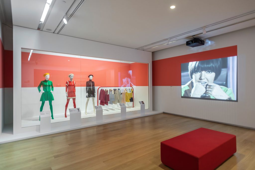 exhibition display of mannequins adjacent to a screen showing film of Mary Quant