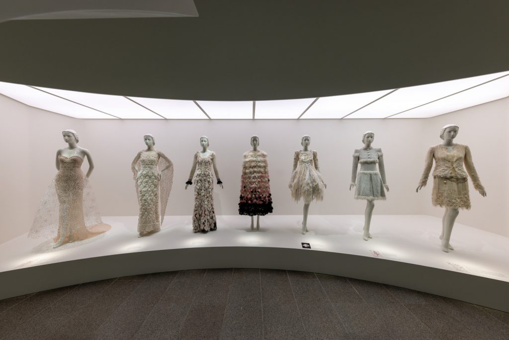 Six cream dresses are worn on white mannequins in an alcove display. The ceiling is fully fitted with a lighting box.