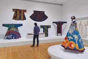 A man looks at kimonos and skirts displayed in a T formation, against a white wall and on a white plinth.