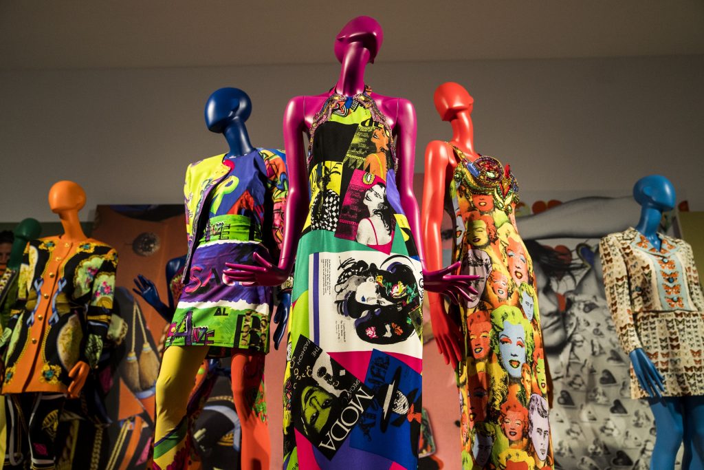 An upwards view of three differently coloured mannequins - blue, burgundy and orange - wearing colourful printed dresses.