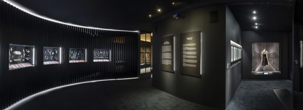 A black gallery view showing jewellery in four cases. Two large labels entitled 'A Chanel Hallmark' and 'Creative Forces' sit in the centre.