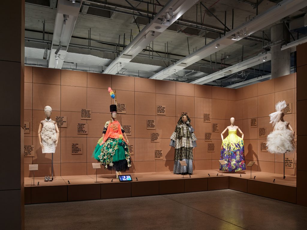 Five dresses are displayed in front of a brown wall in the 'Start Up Culture' room.