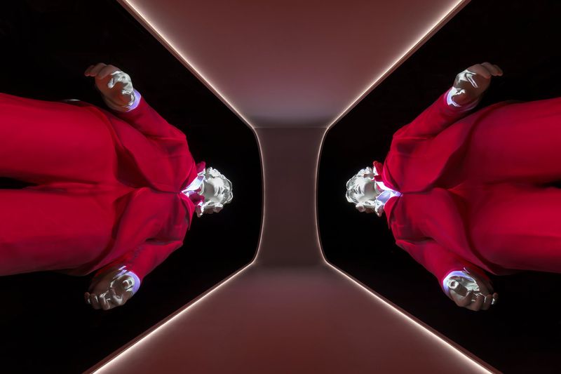Exhibition display of mirrored figure of 2 male mannequins in red suit taken from below