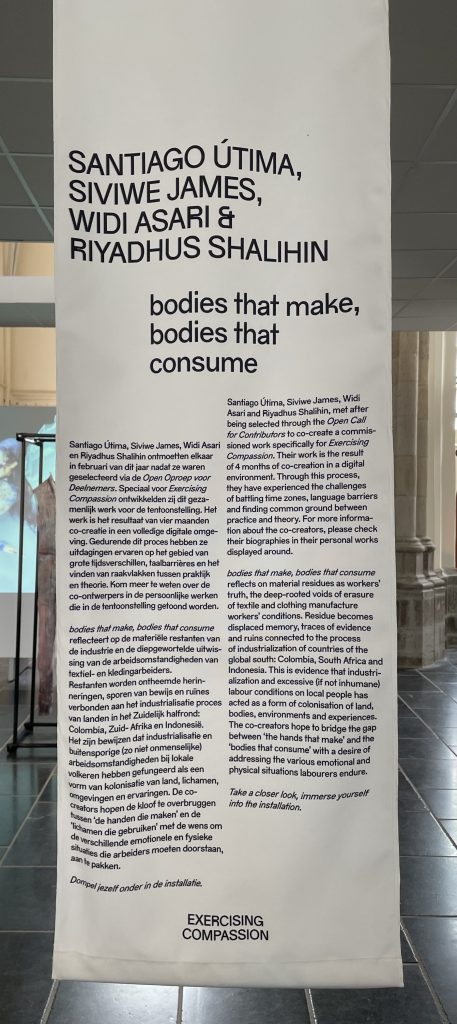A long label, printed on fabric, hangs from the ceiling. The title reads 'Santiago Utima, Siviwe James, Widi Asari & Riyadhus Shalihin - bodies that make, bodies that consume'
