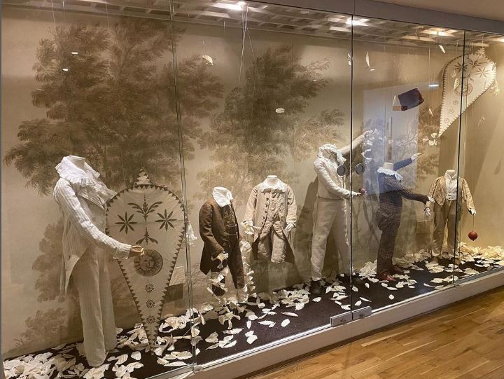A row of boys' dress on display. One mannequin holds a kite whilst another holds a conquer on a string. Another kit is 'flying' in the case.