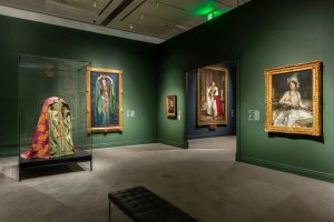 “Fashioned by Sargent” installation view. Far left, ‘‘Beetle Wing Dress’’ for Lady Macbeth. Sargent’s painting of the actress Ellen Terry as Lady Macbeth, in the shimmering gown (which boasts actual beetle wing cases affixed to its surface), hangs nearby. The dress was created by Alice Laura Comyns-Carr.Credit: Museum of Fine Arts, Boston