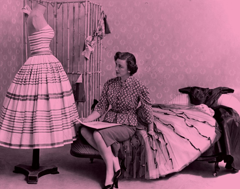 Pink 1950's dress on mannequin with lady perched on a bed.