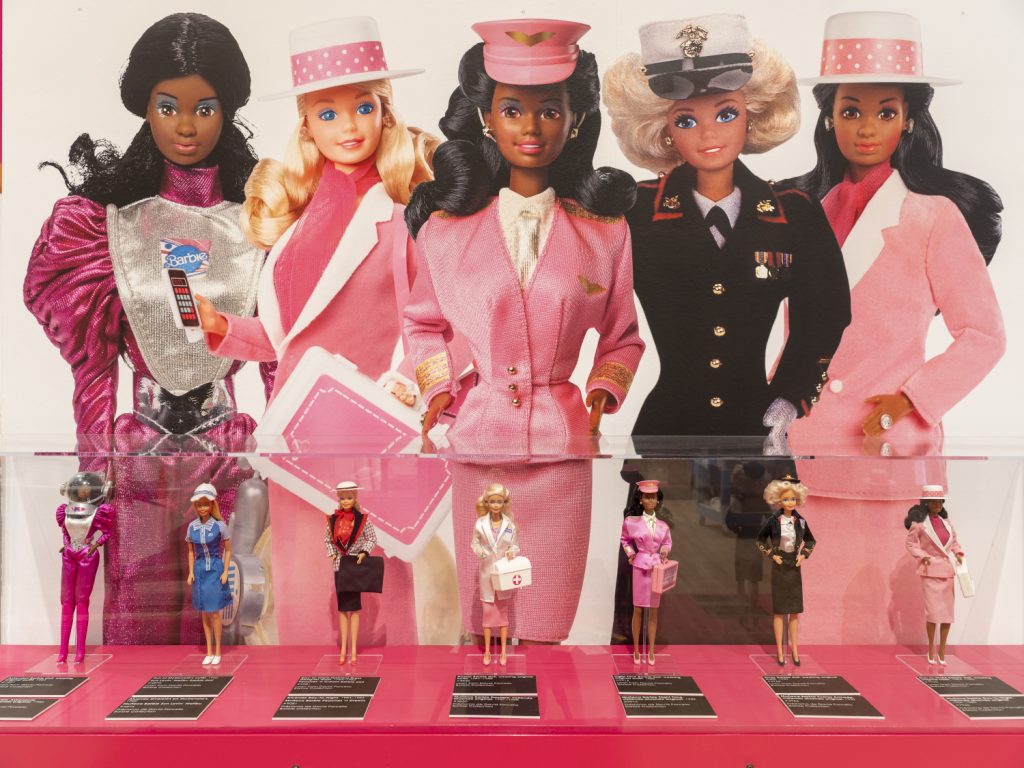 A display of 8 Barbie dolls in pink uniform, matching hats and accessories.