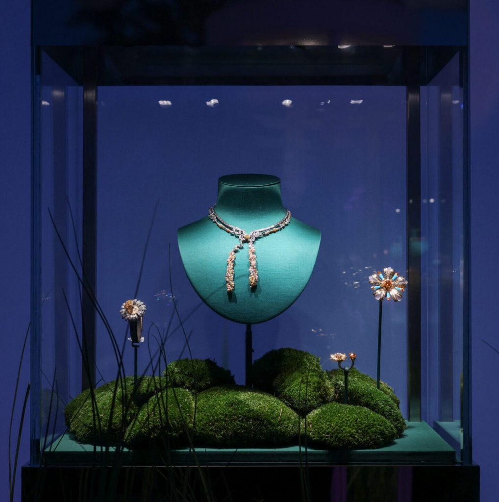 A yellow and silver chain necklace on display. Display is arranged as if the necklace is on a green piece of grass and against a night time blue sky.