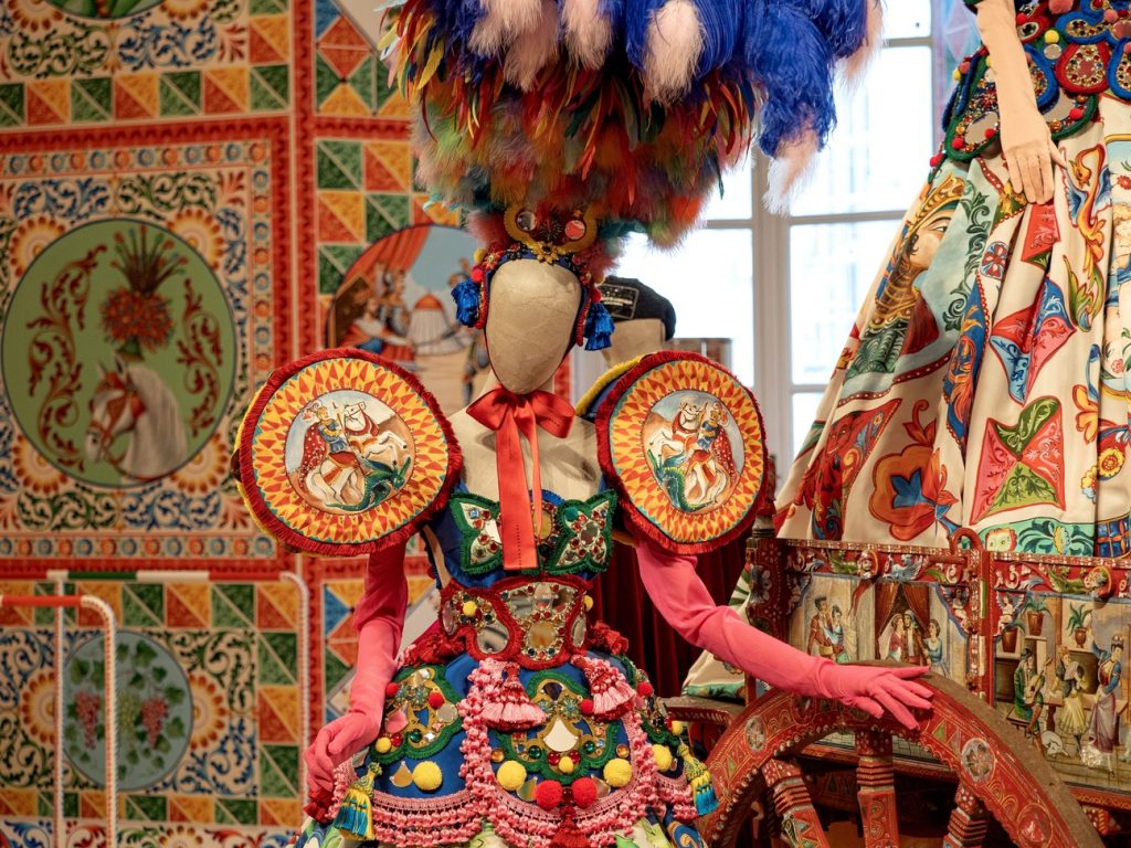 A colourful female mannequin in hues of blue, pink, orange, red and yellow. Feather hat with red, white and yellow.