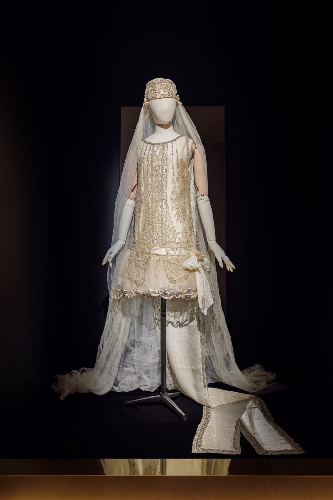 A 1920's white wedding gown with a veil complete with gold embellishments.