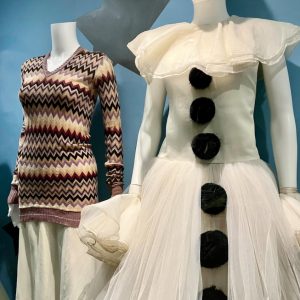 Two female mannequins, one dressed in a patterned sweater and a white with black buttons dress