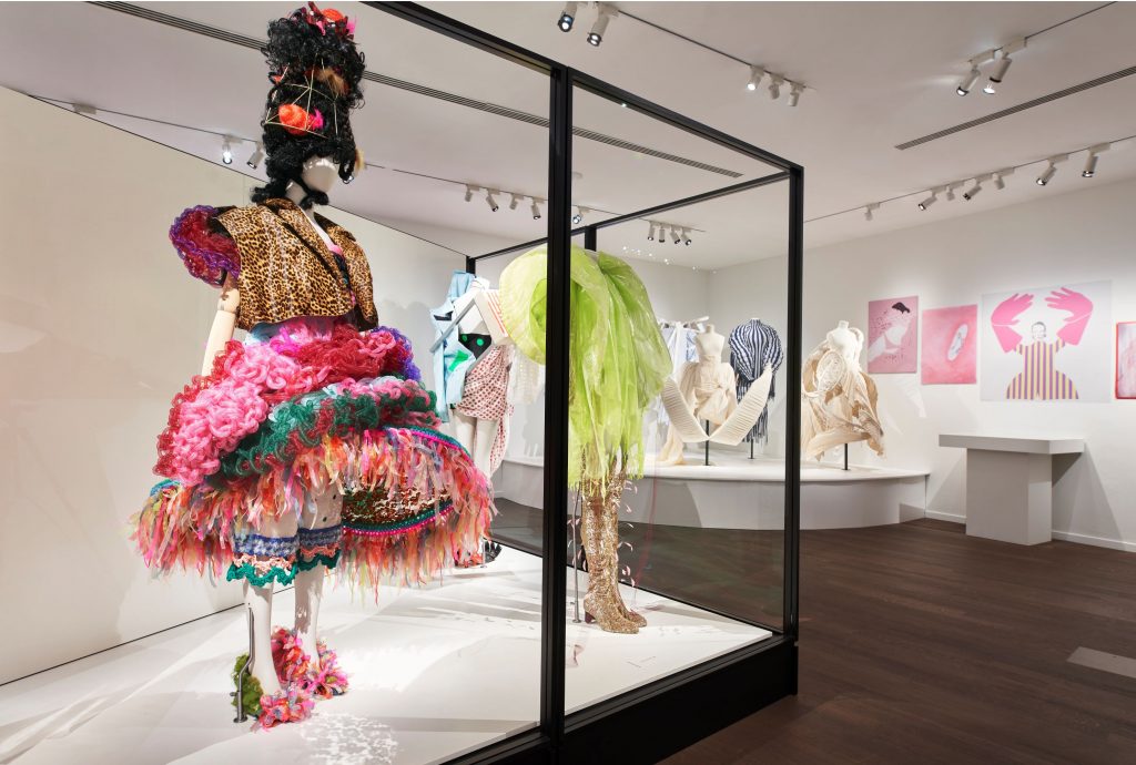 Three mannequins on display wearing female garments. Left: Mannequin wearing a gold and pink, multi-coloured top and skirt. Middle: wearing a green dress.