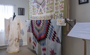 A collection of textiles with a colourful pattern. Female mannequin wearing a white outfit.