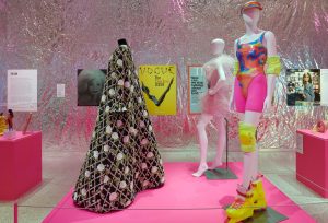 A pink display of three female mannequins dressed in one black floor length piece and two colourful pink outfits